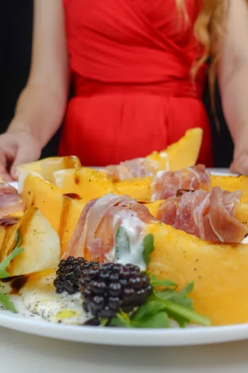 Helena is standing next to a plate with Melon Prosciutto Burrata Salad with balsamic vinegar and blackberries