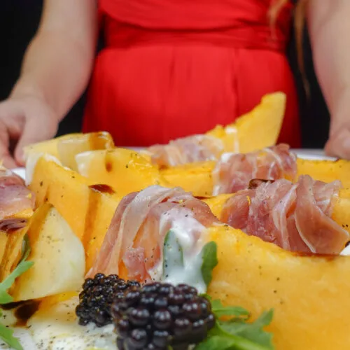 Helena is standing next to a plate with Melon Prosciutto Burrata Salad with balsamic vinegar and blackberries