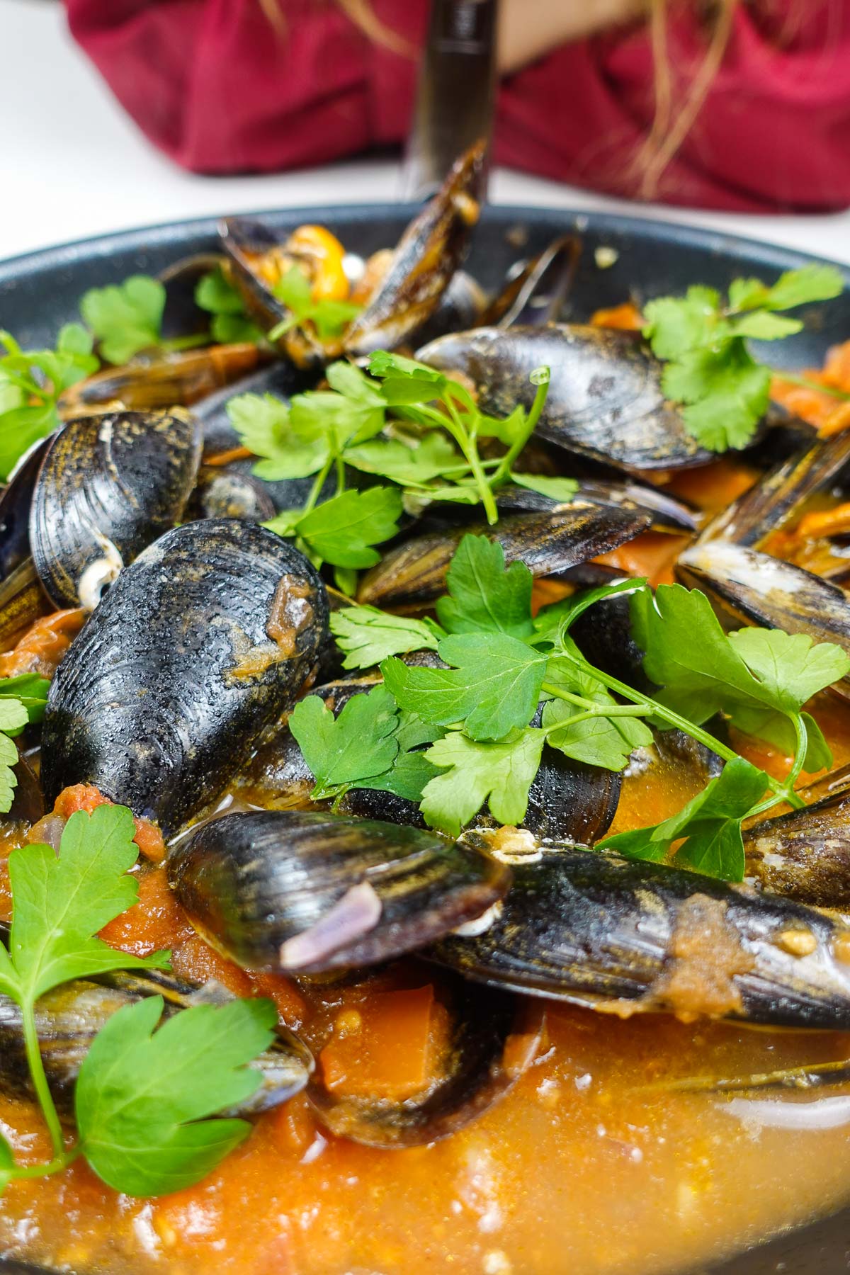 Helena is standing behind the pan full with mussels in tomato sauce