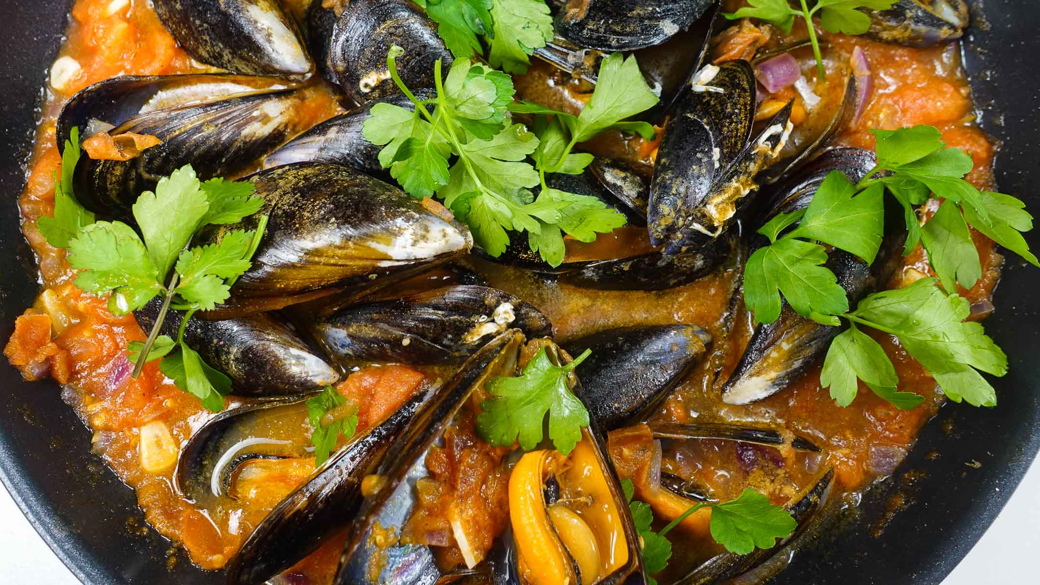 A pan filled with hot Mussels in tomato sauce