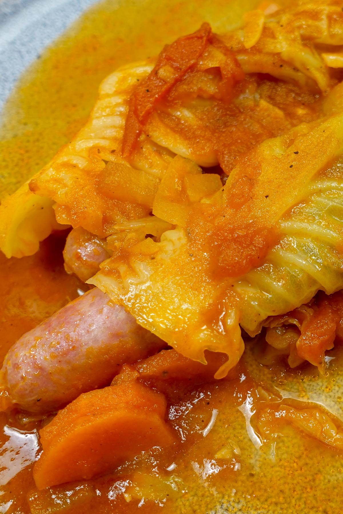 A closeup of plate with two sausages with cabbage and a lot of sauce around