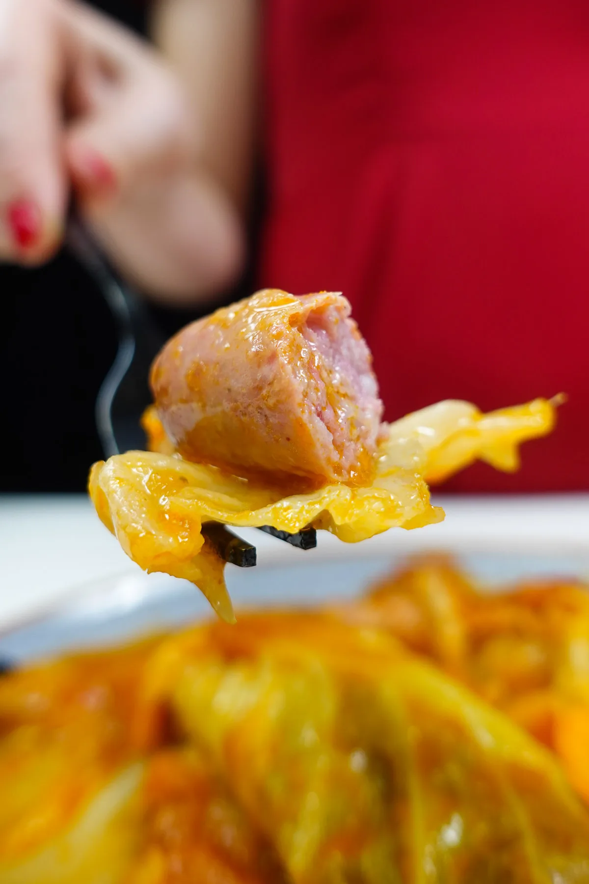 Helena is holding a fork with cabbage and sausage on top