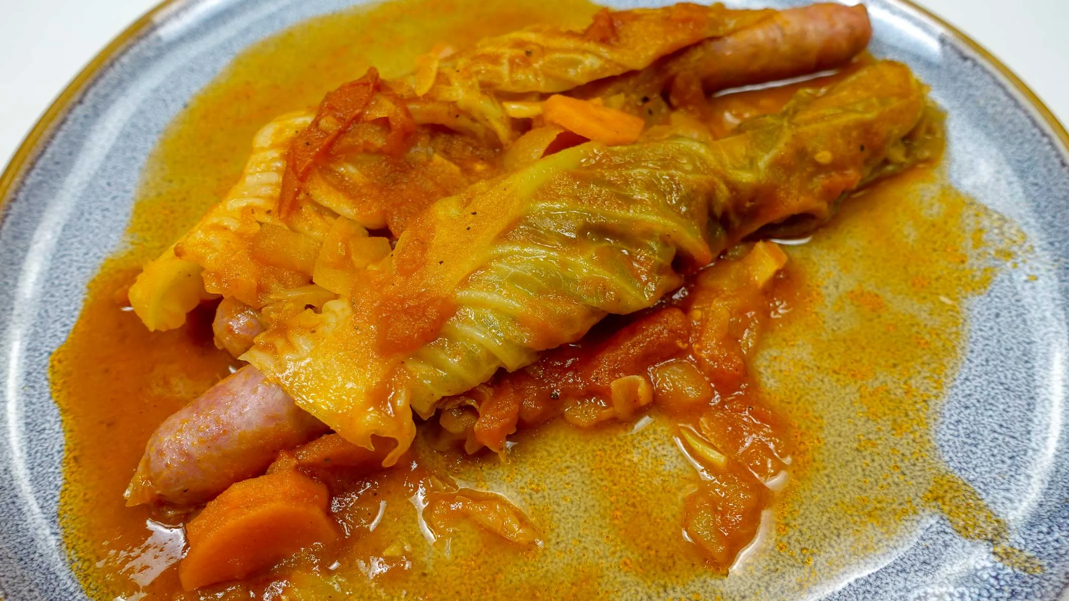 A blue plate with two sausages with cabbage and sauce around