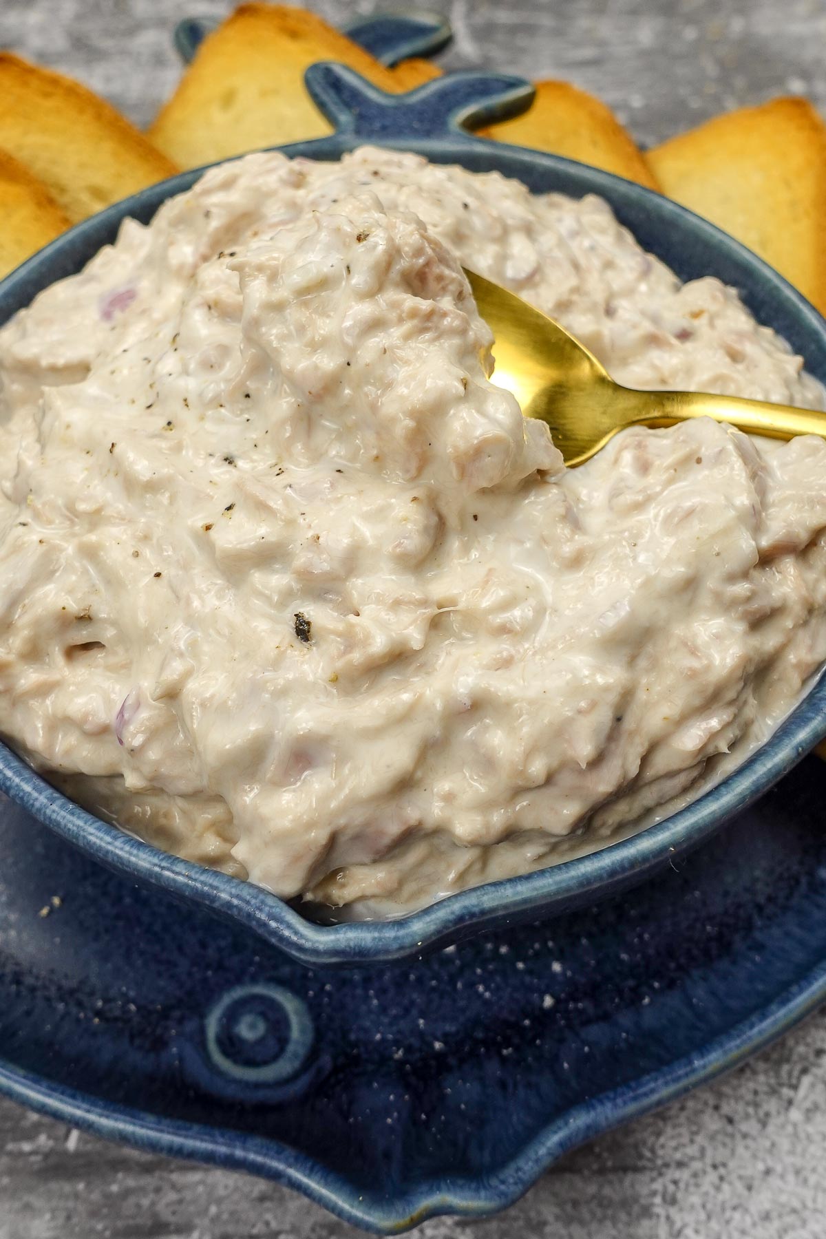 Tuna dip in a beautiful blue bowl with crackers in a side.