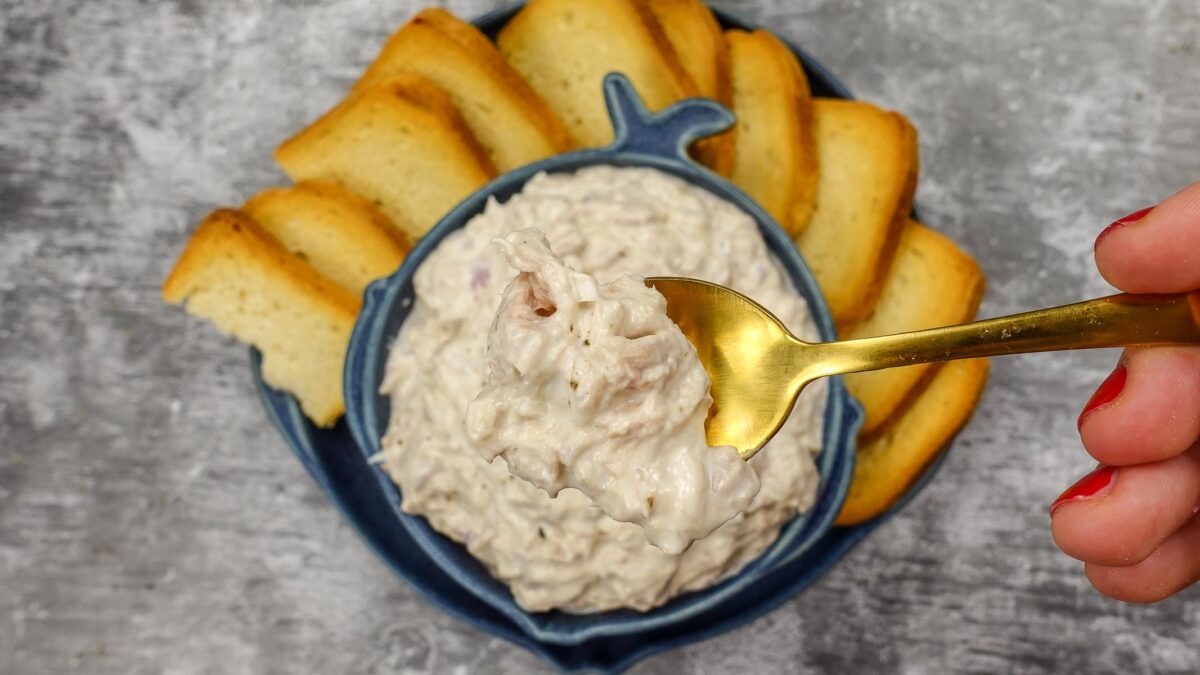 Helena is holding a spoonful with tuna dip over the bowl with tuna dip.