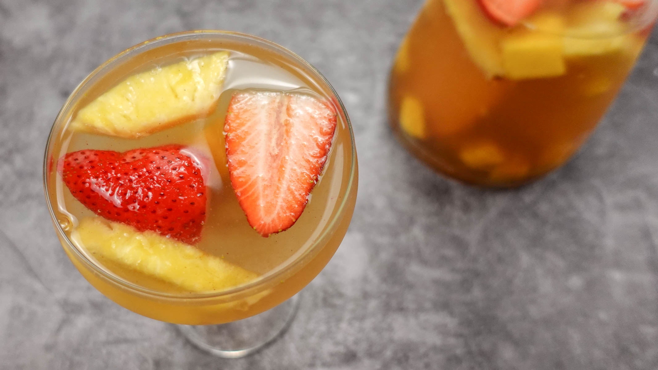 A glass and a jar of white sangria on a table