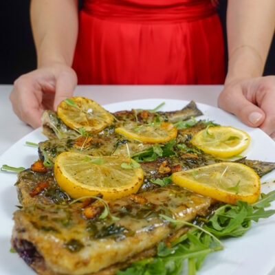 Helena is holding a white plate with mouthwatering Trout in Lemon Garlic Sauce