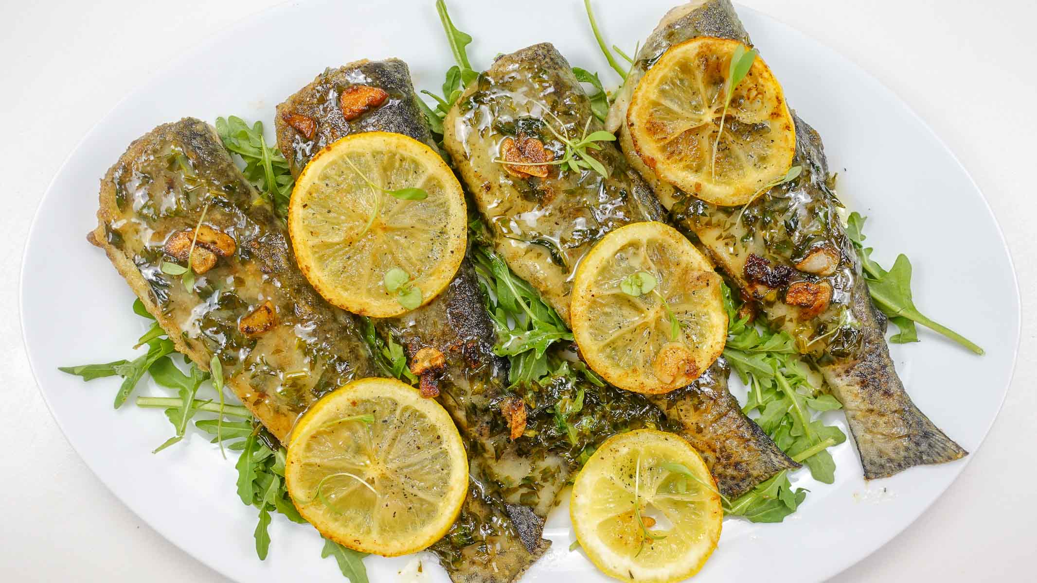 A photo of a plate with Trout in Lemon Garlic Sauce and slices of lemon