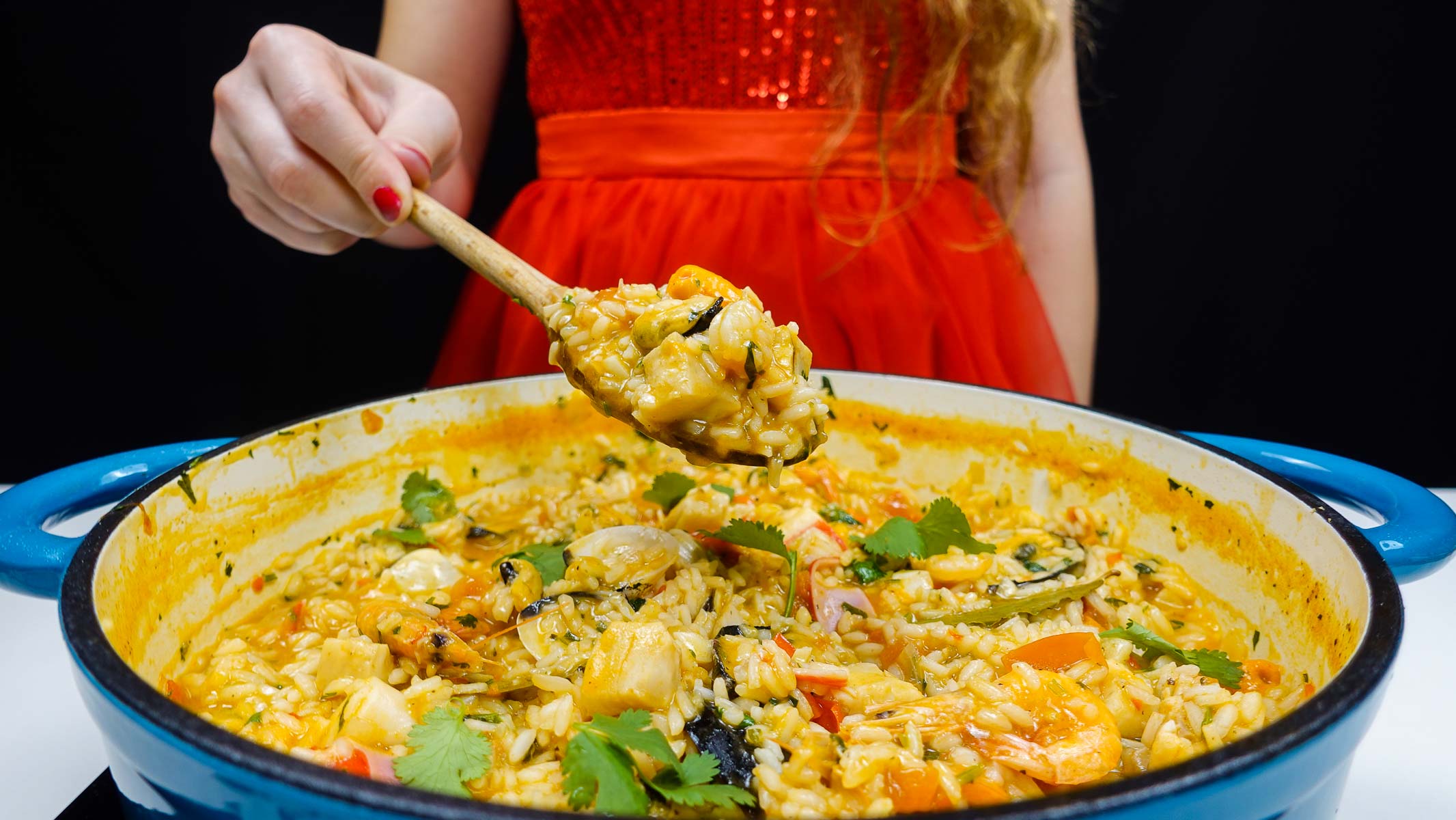 A big blue pot of seafood rice and Helena is holding a spoon over the pot