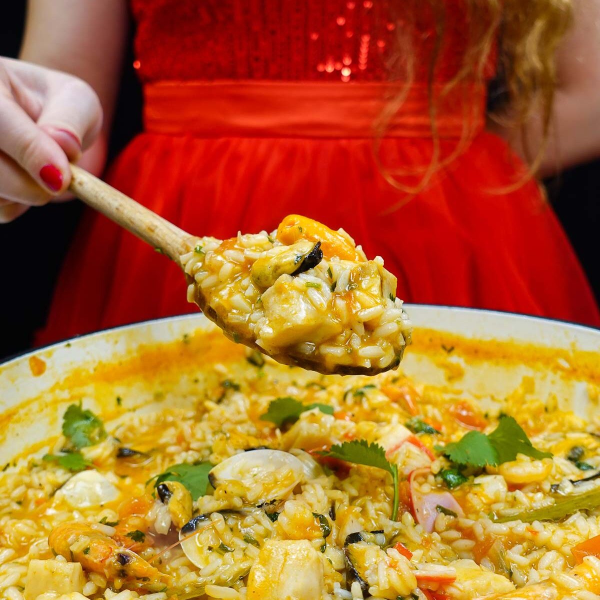Helena is standing behind and holding a spoon with seafood rice