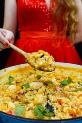 Helena is standing behind and holding a spoon with seafood rice