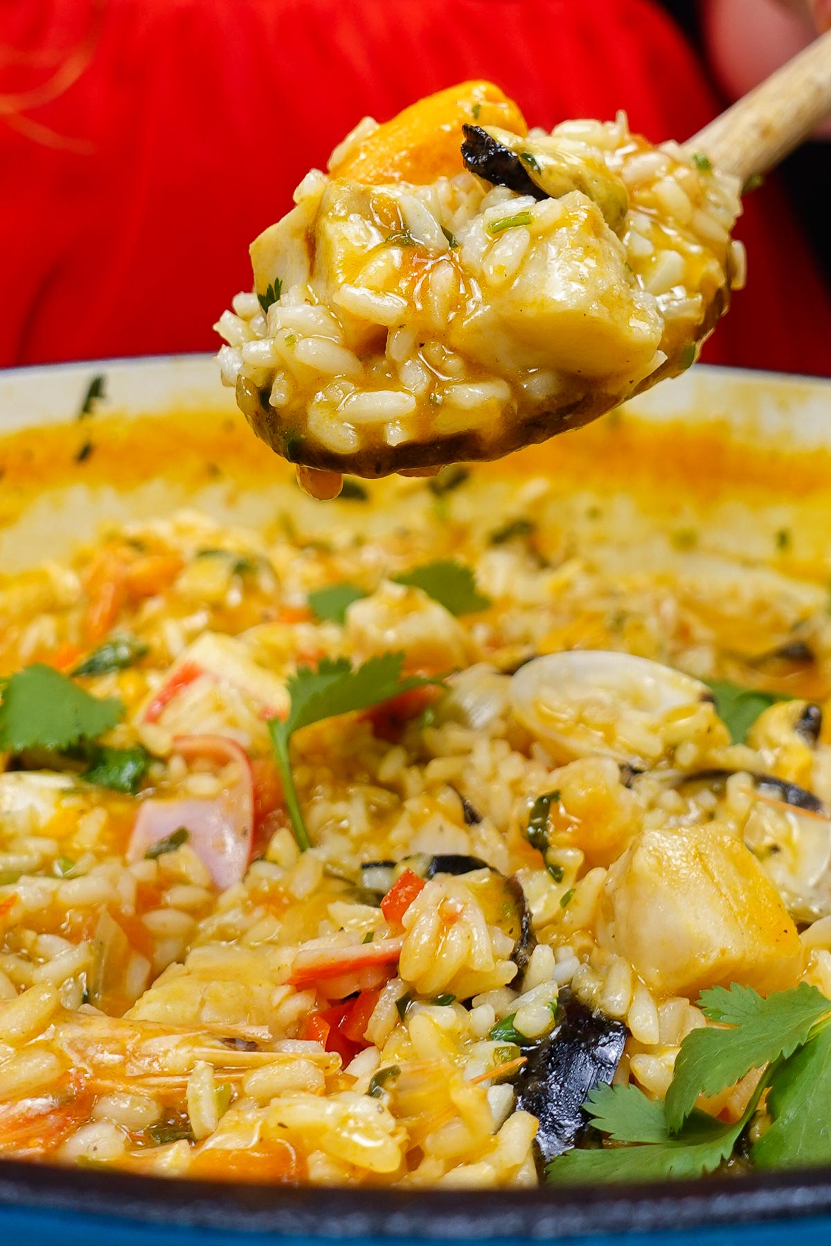 A spoon with Portuguese rice over the blue pot with seafood rice