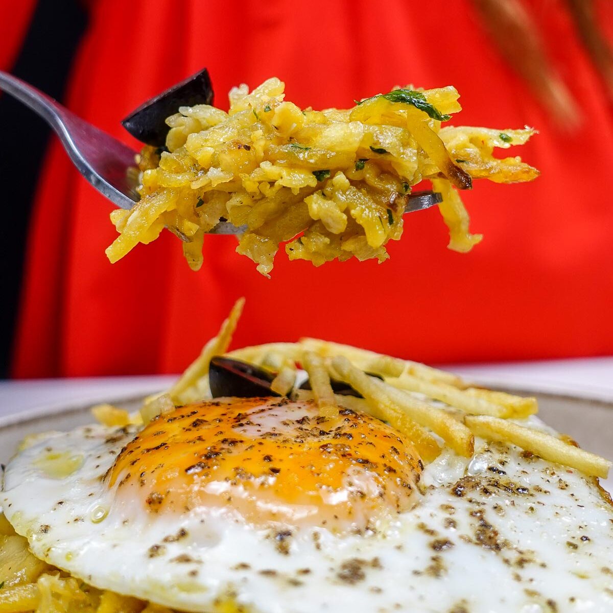 Helena is holding a fork full of cod with potatoes over the plate with bacalhau a bras