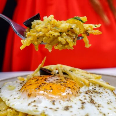 Helena is holding a fork full of cod with potatoes over the plate with bacalhau a bras