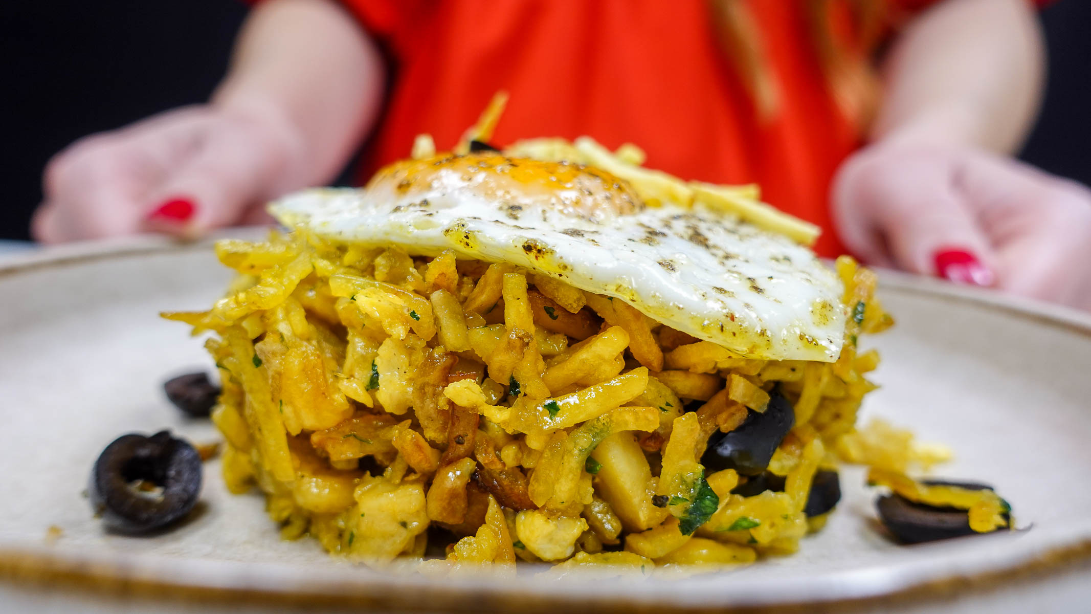 Salt cod with shredded potatoes, black olives, and fried egg on plate.