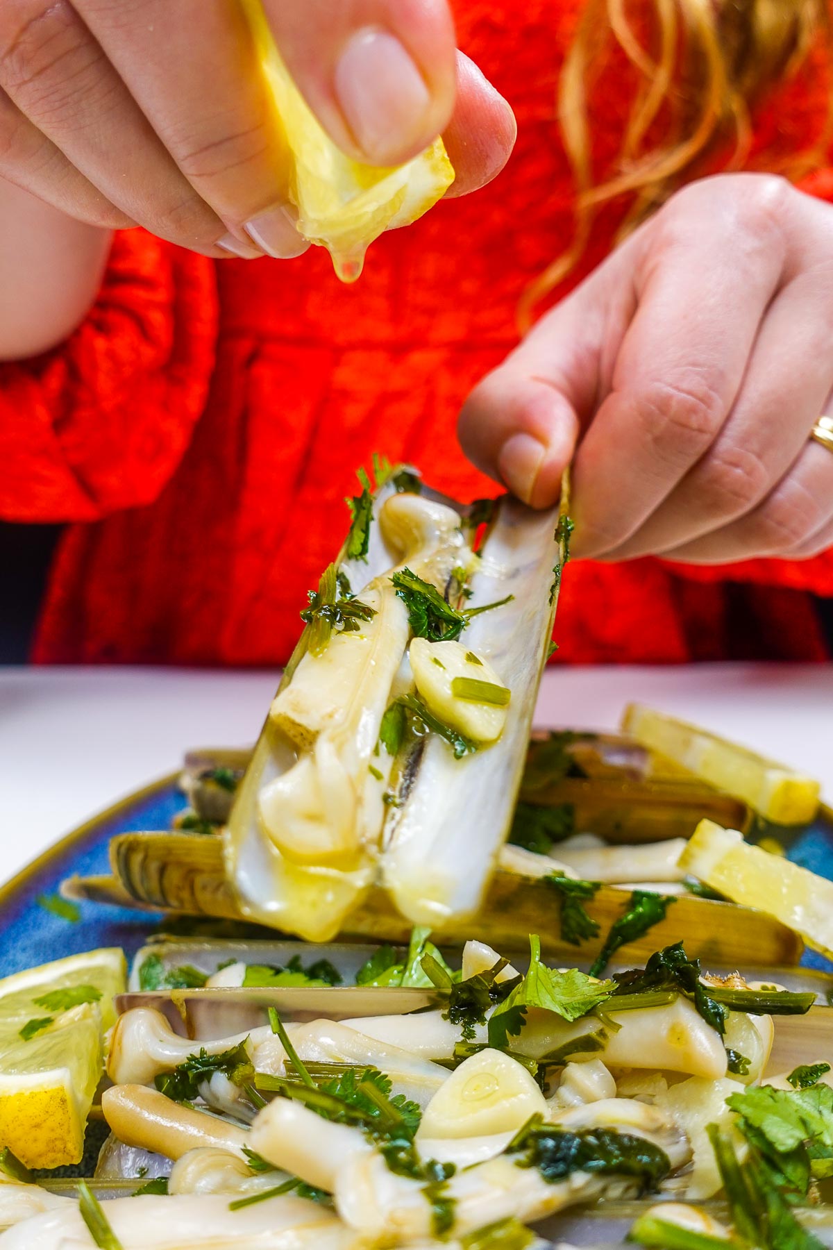 Helena is drizzling lemon juice on one of razor clams over the plate with clams