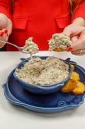 Helena is holding one cracker with sardine pate on top and a spoon full of sardine pate
