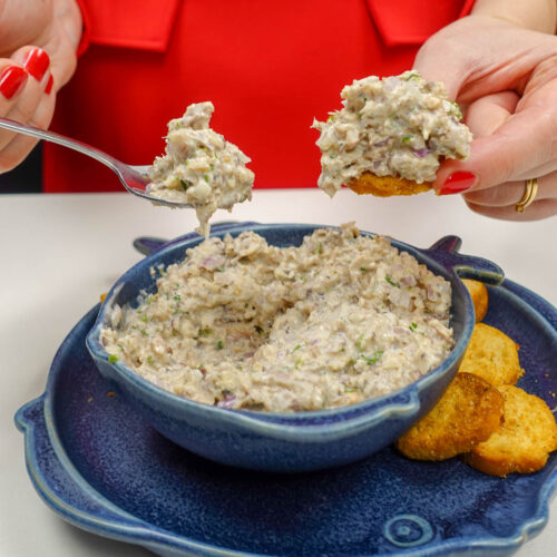 Helena is holding one cracker with sardine pate on top and a spoon full of sardine pate