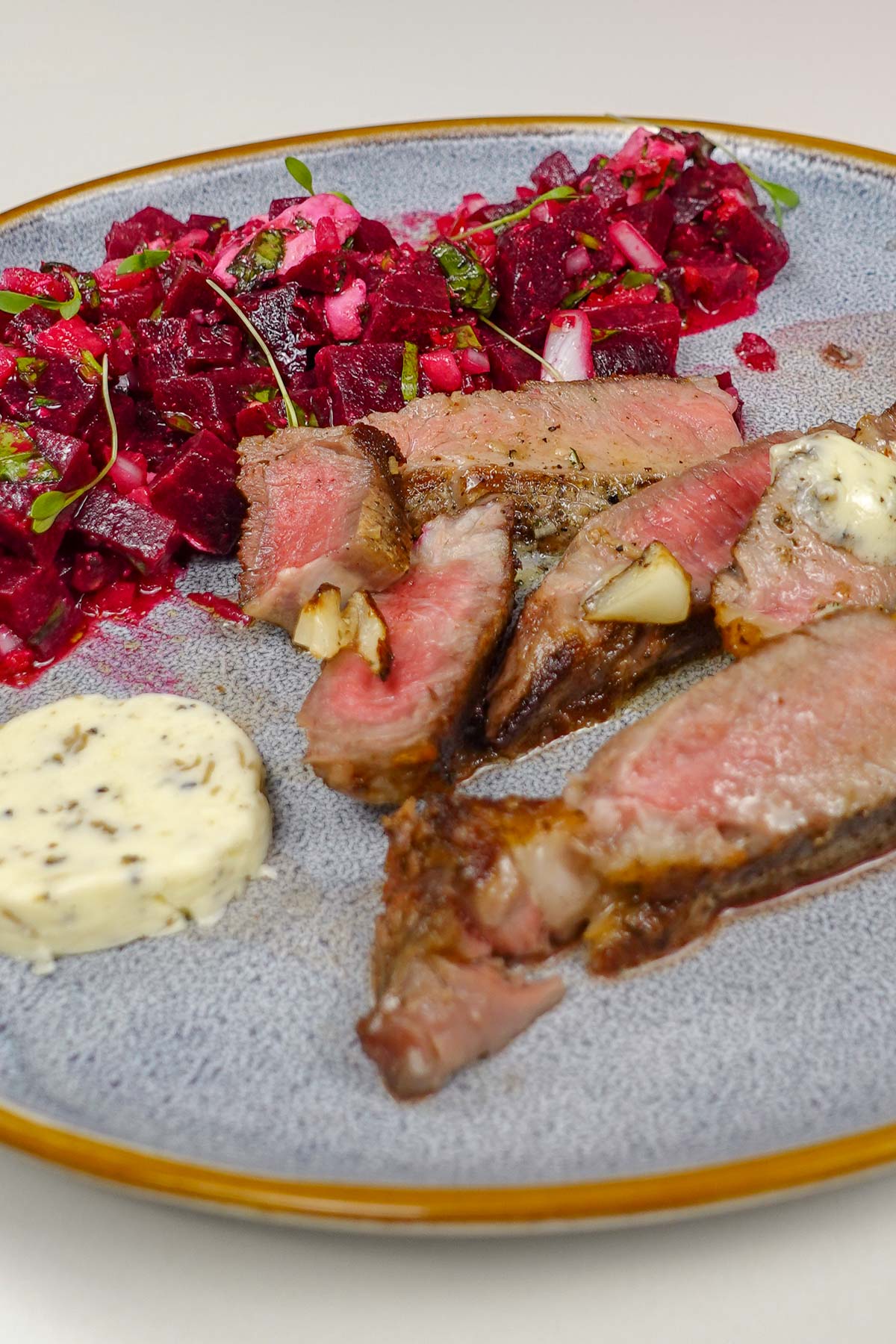 Steak with black truffle butter on a blue plate and beetroot feta salad on a side.