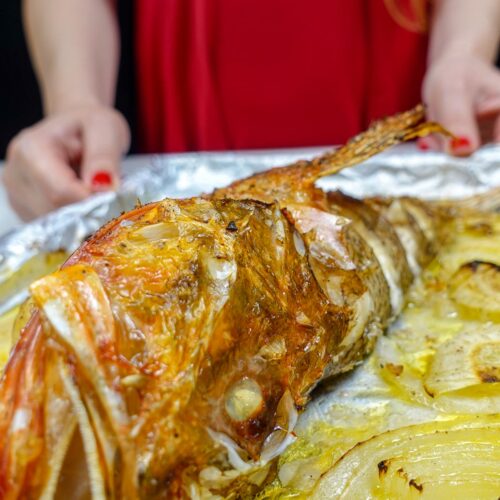Helena is holding a tray of ready baked Mediterranean Scorpionfish with onions and lemon.