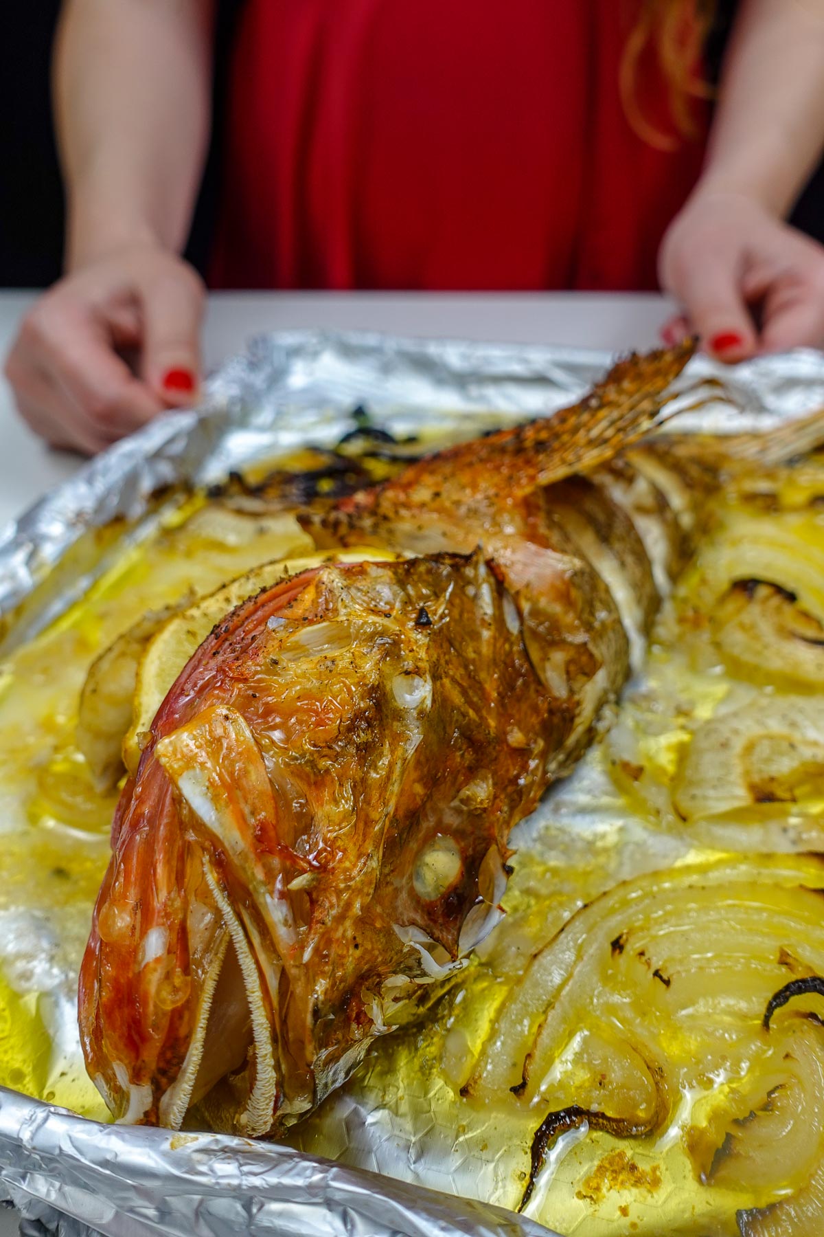 Helena is holding a tray with Mediterranean Baked Scorpionfish with lemon and onion.