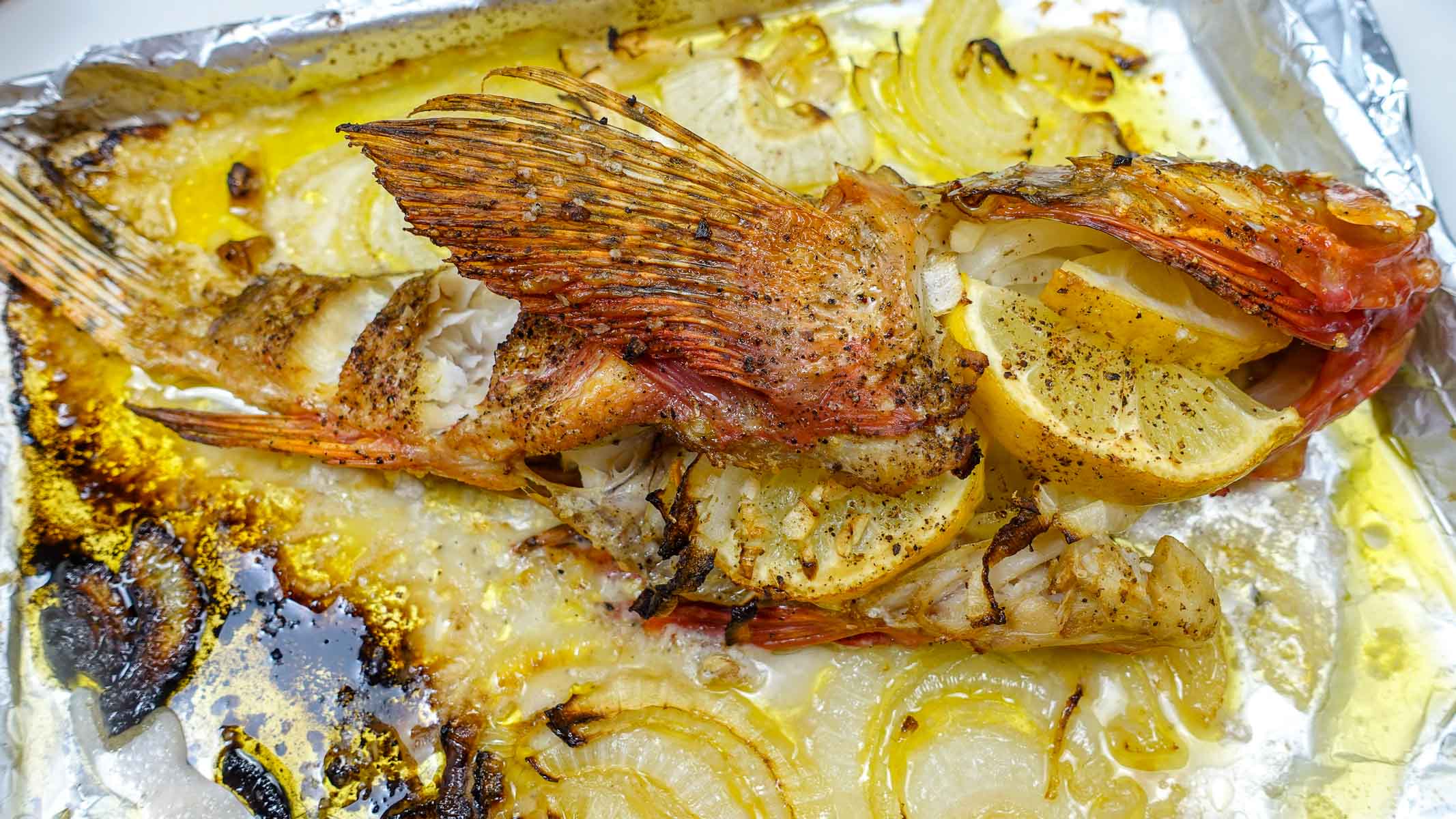 A tray with Mediterranean Baked Scorpionfish with lemon and onion with the view on top.