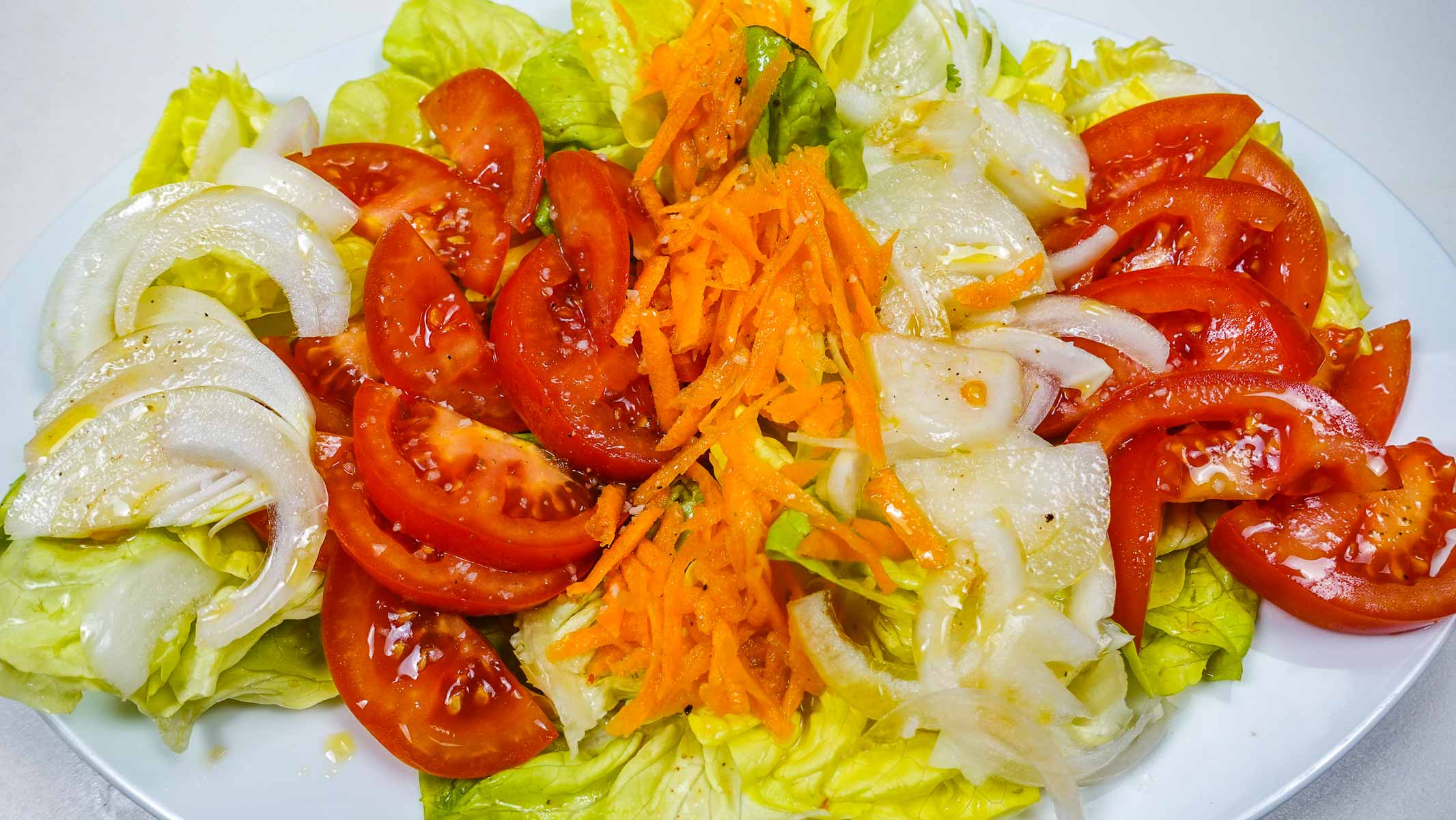 A white plate of juicy and delicious Portuguese mixed salad on a white table.