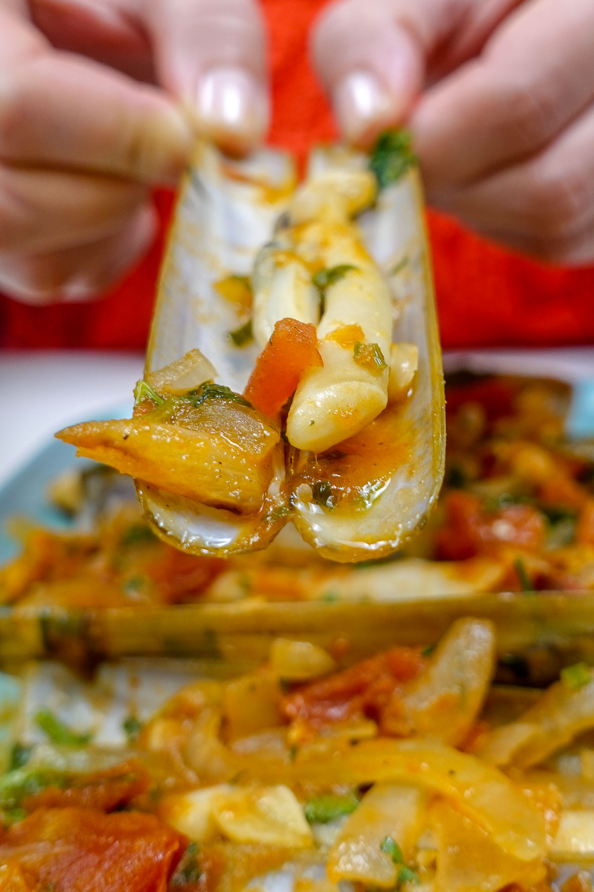 Helena is holding one razor clam with tomatoes and small pieces of garlic inside clam