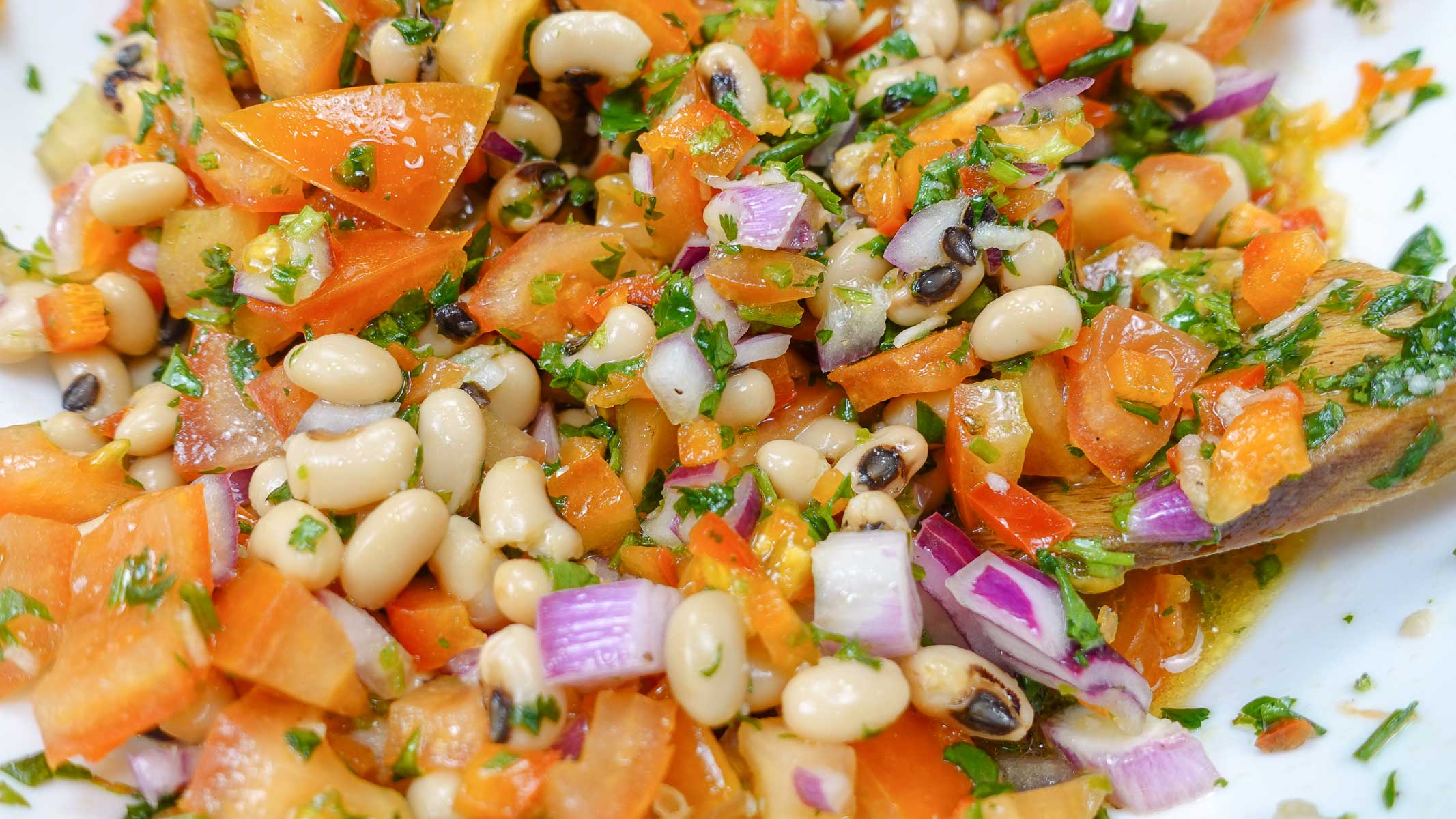 A closeup of ready black eyed peas with a wooden spoon inside.