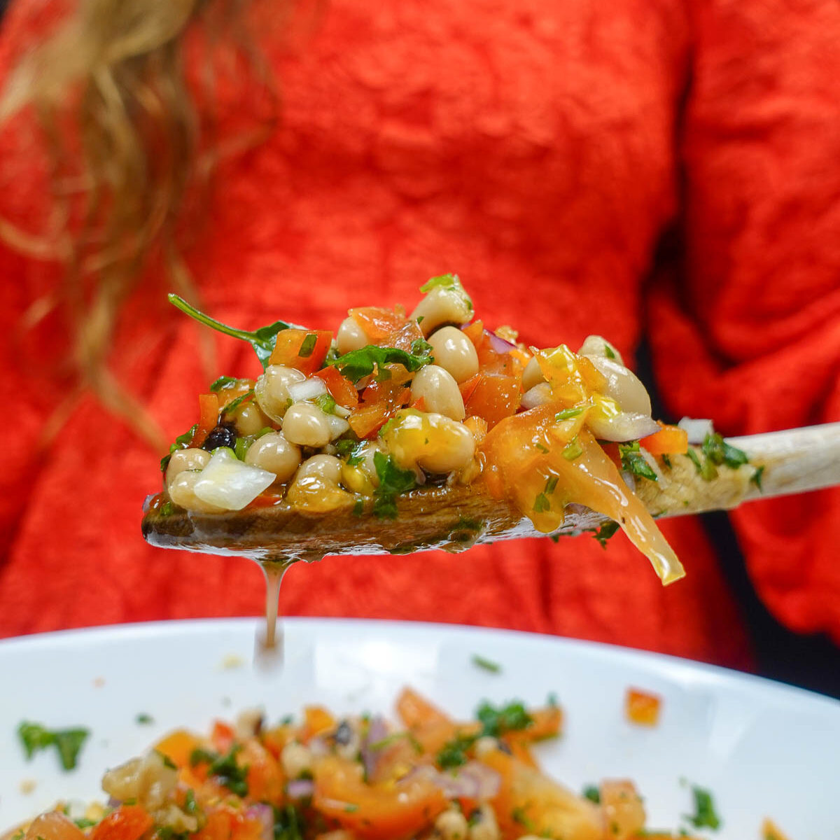 Helena is holding a big spoon with black eyed peas over the bowl with juicy salad.