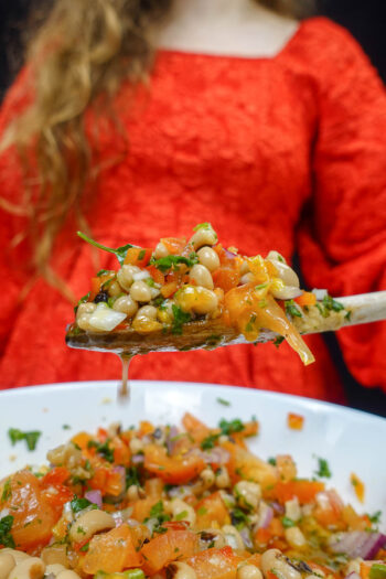 Helena is holding a big spoon with black eyed peas over the bowl with juicy salad.