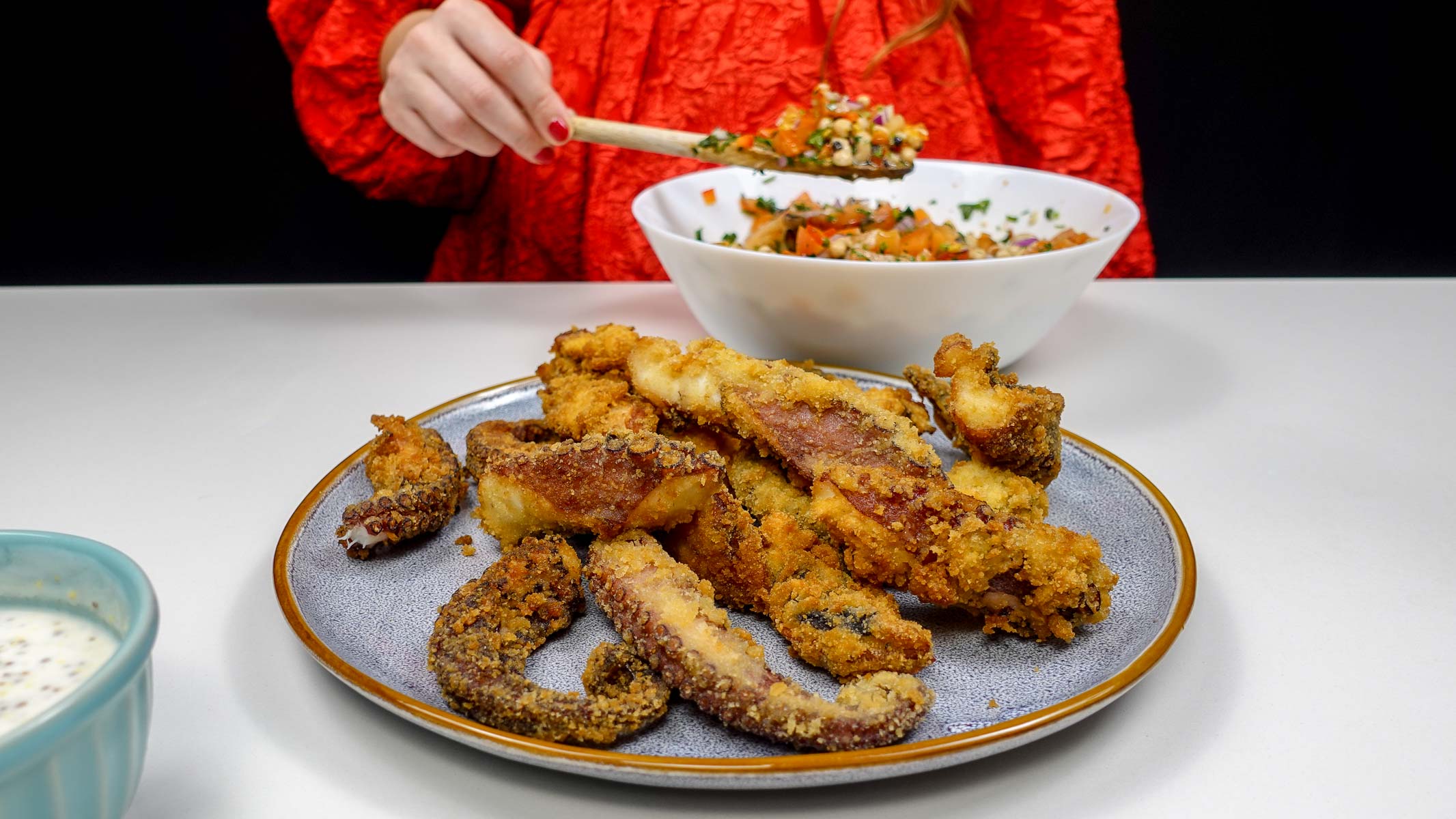 Crispy Portuguese fried octopus tentacles on a plate with a bowl of salad and Helena is holding a spoon of salad.