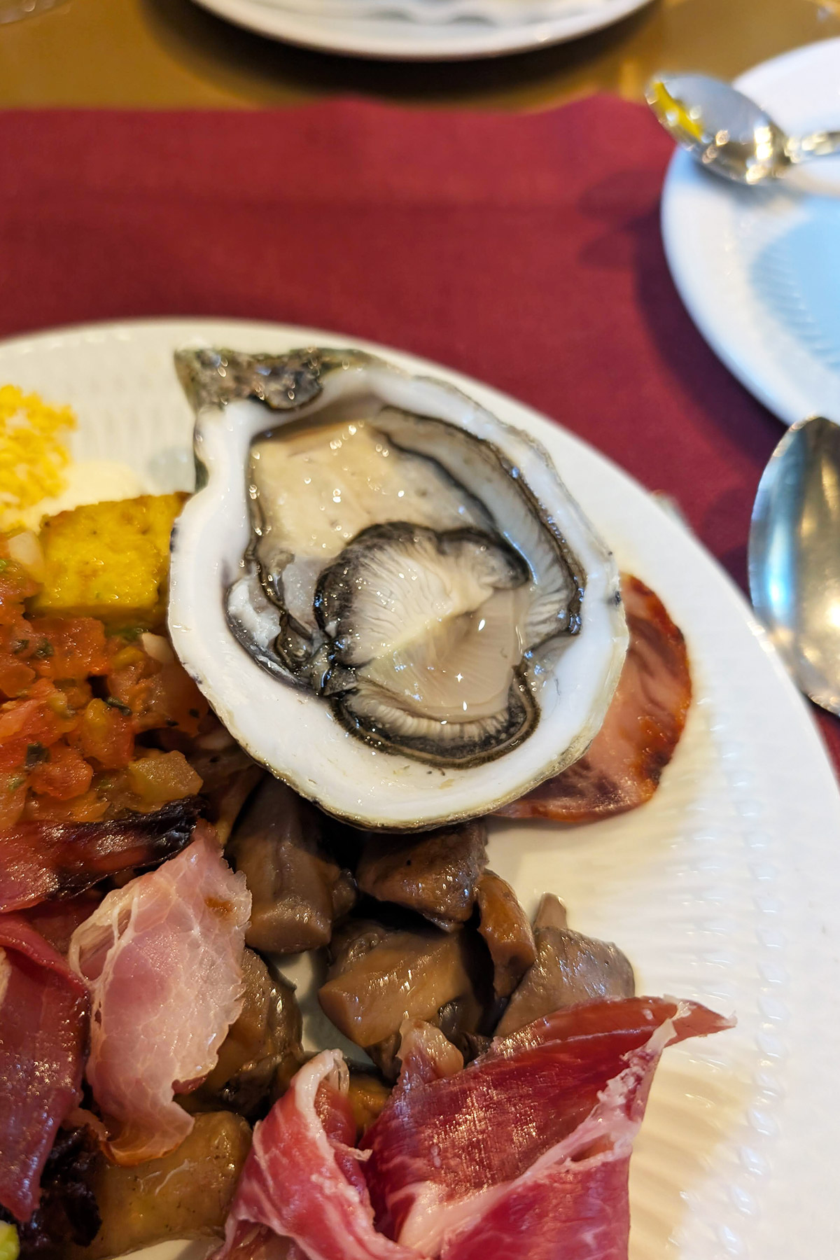 Fresh oyster with cured meats and sautéed mushrooms on white plate.