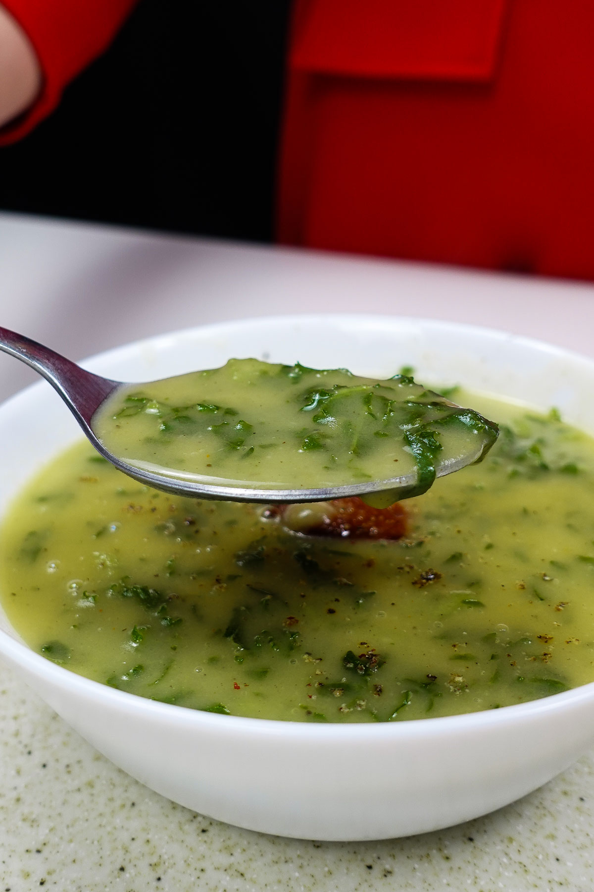 Creamy Portuguese potato kale soup in white bowl with spoon.