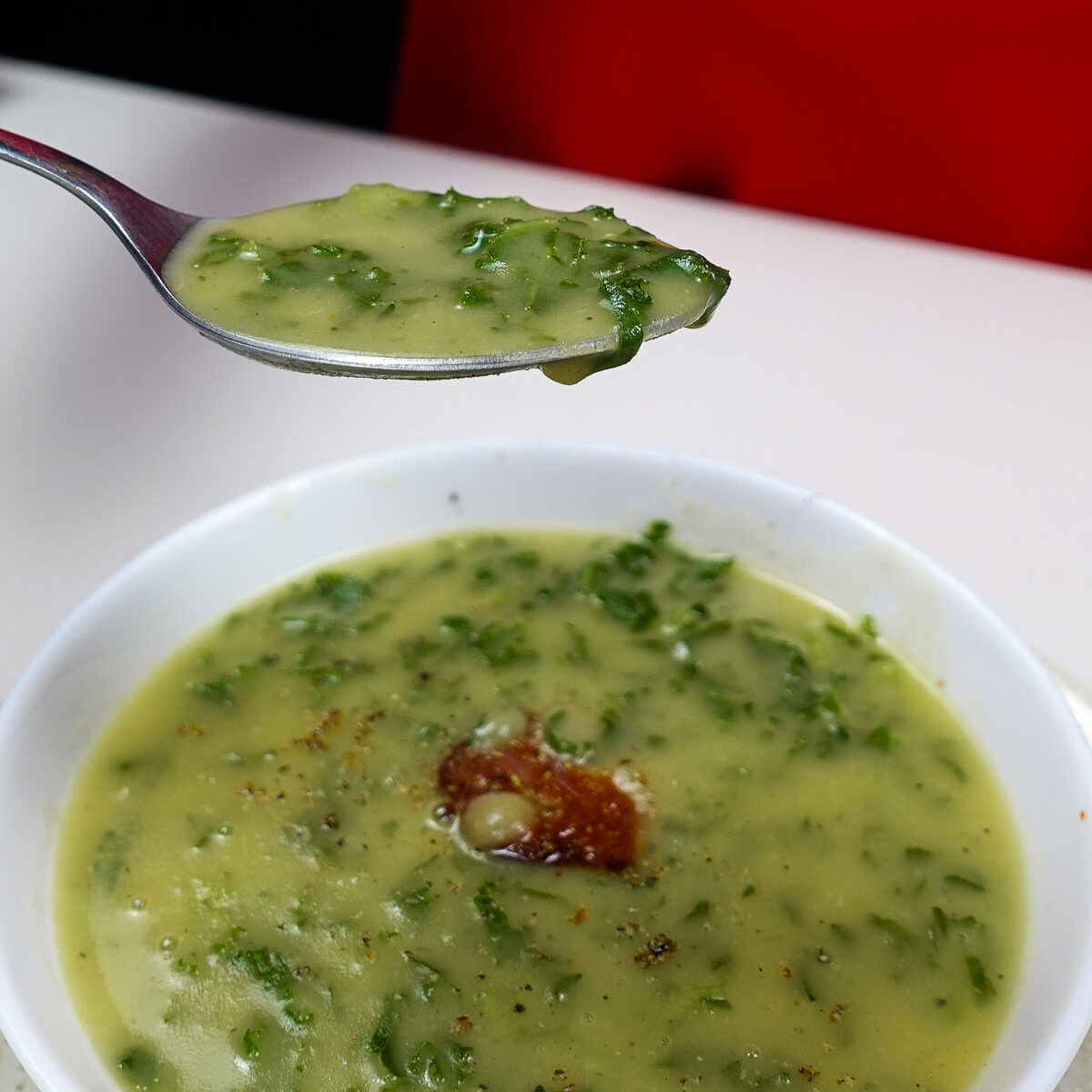 Bowl of creamy potato kale soup with chorizo and spoonful lifted.