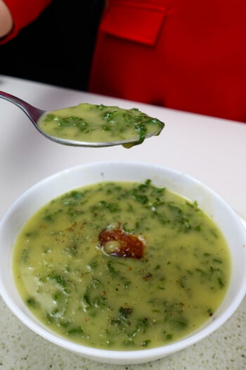 Bowl of creamy potato kale soup with chorizo and spoonful lifted.