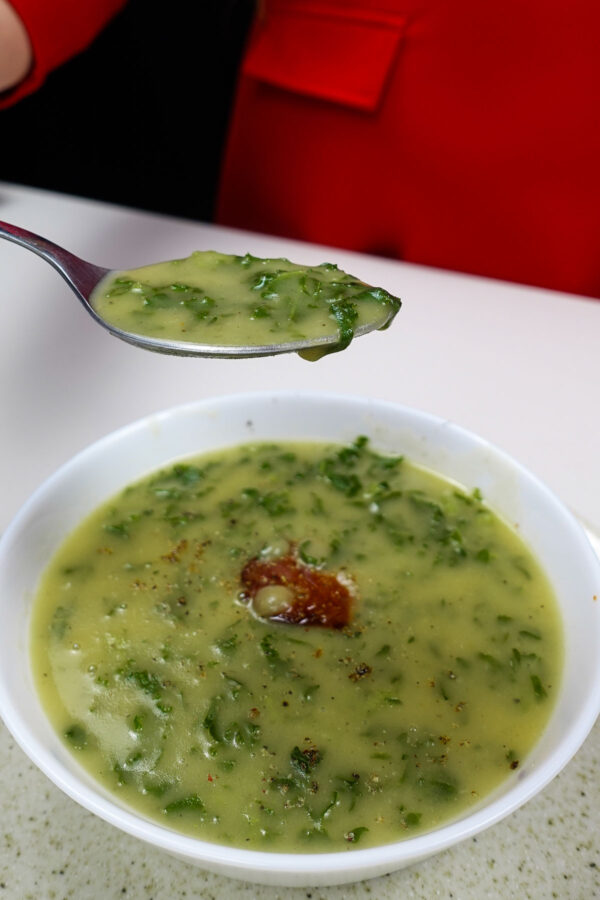 Bowl of creamy potato kale soup with chorizo and spoonful lifted.