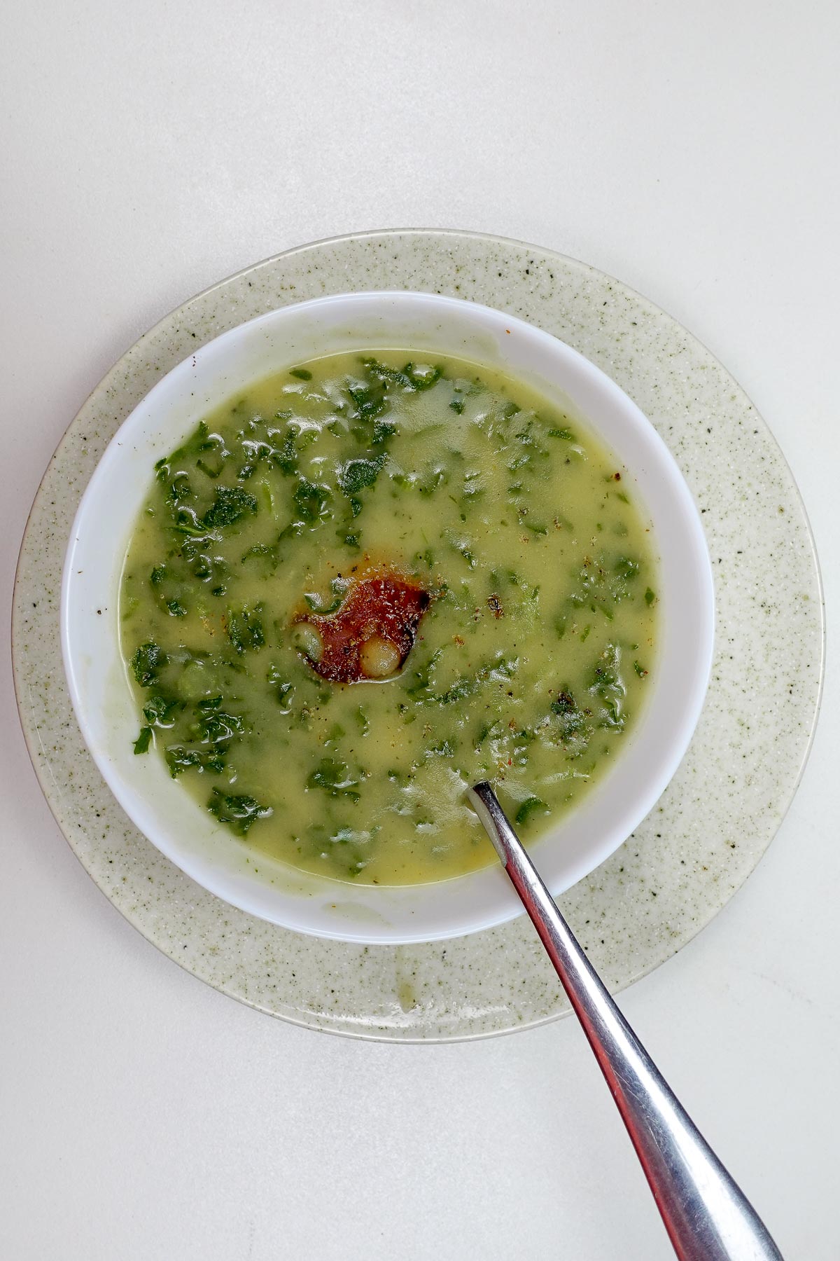 Bowl of Portuguese potato kale soup with chorizo slice and spoon.