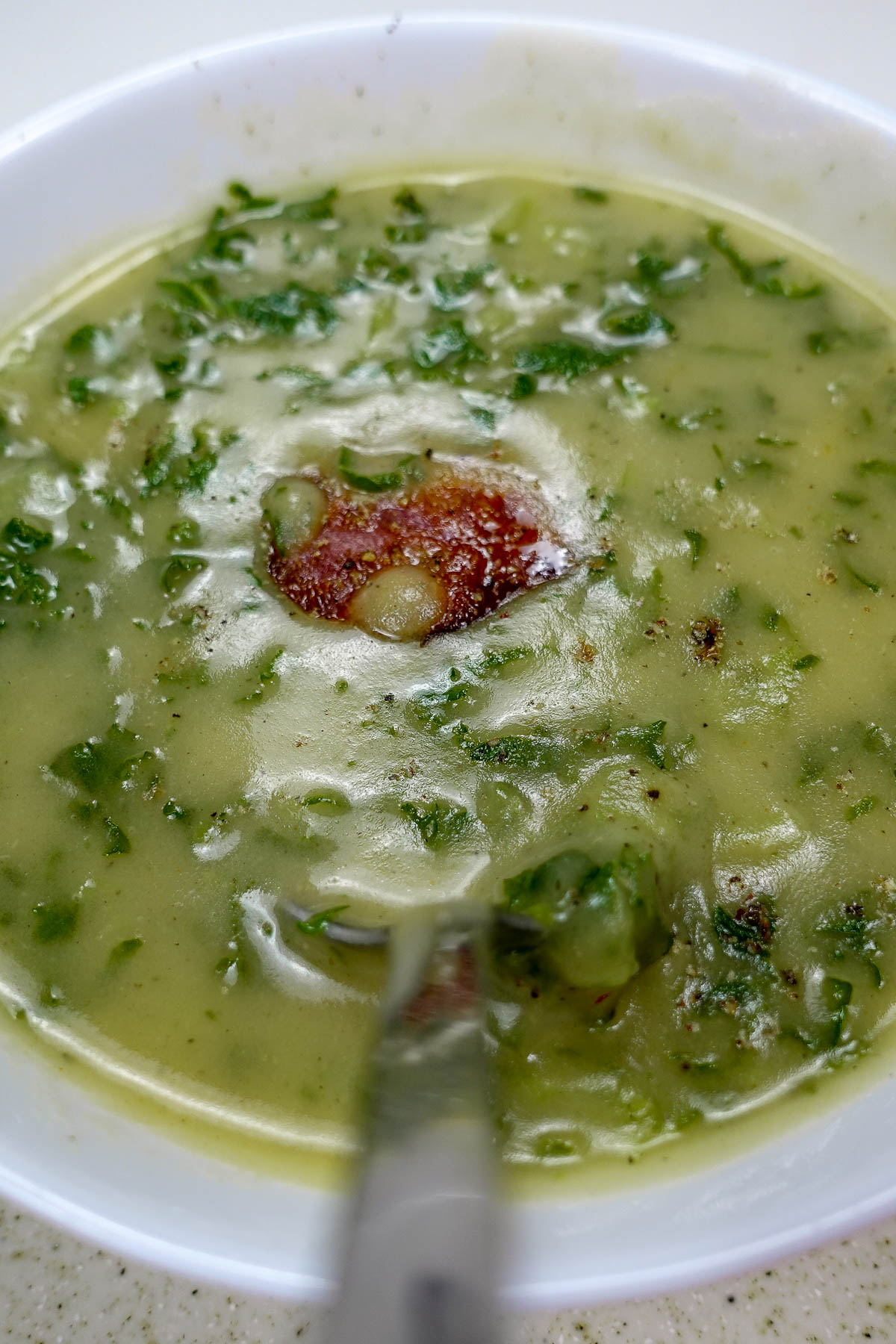Bowl of creamy Portuguese potato kale soup with chorizo slice.