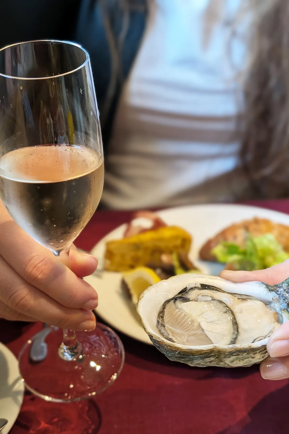 Helena holding an oyster and a glass of champagne on a red tablecloth.