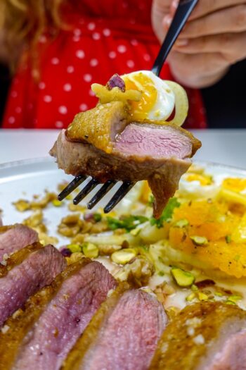 Helena is holding a black fork with crispy duck breast with soft boiled egg and fennel orange salad.