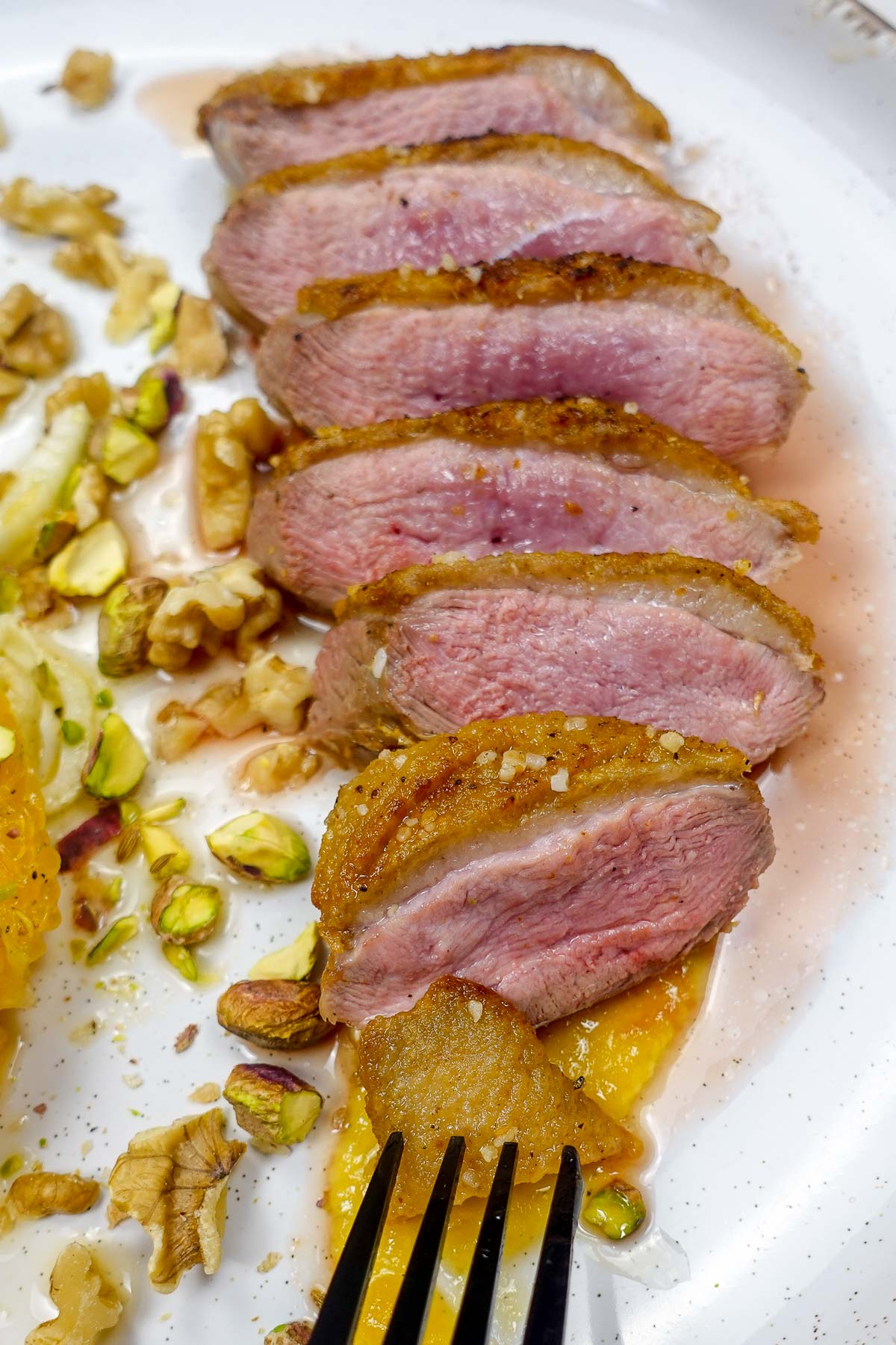 Sliced crispy duck breast with nuts and orange slices on plate.