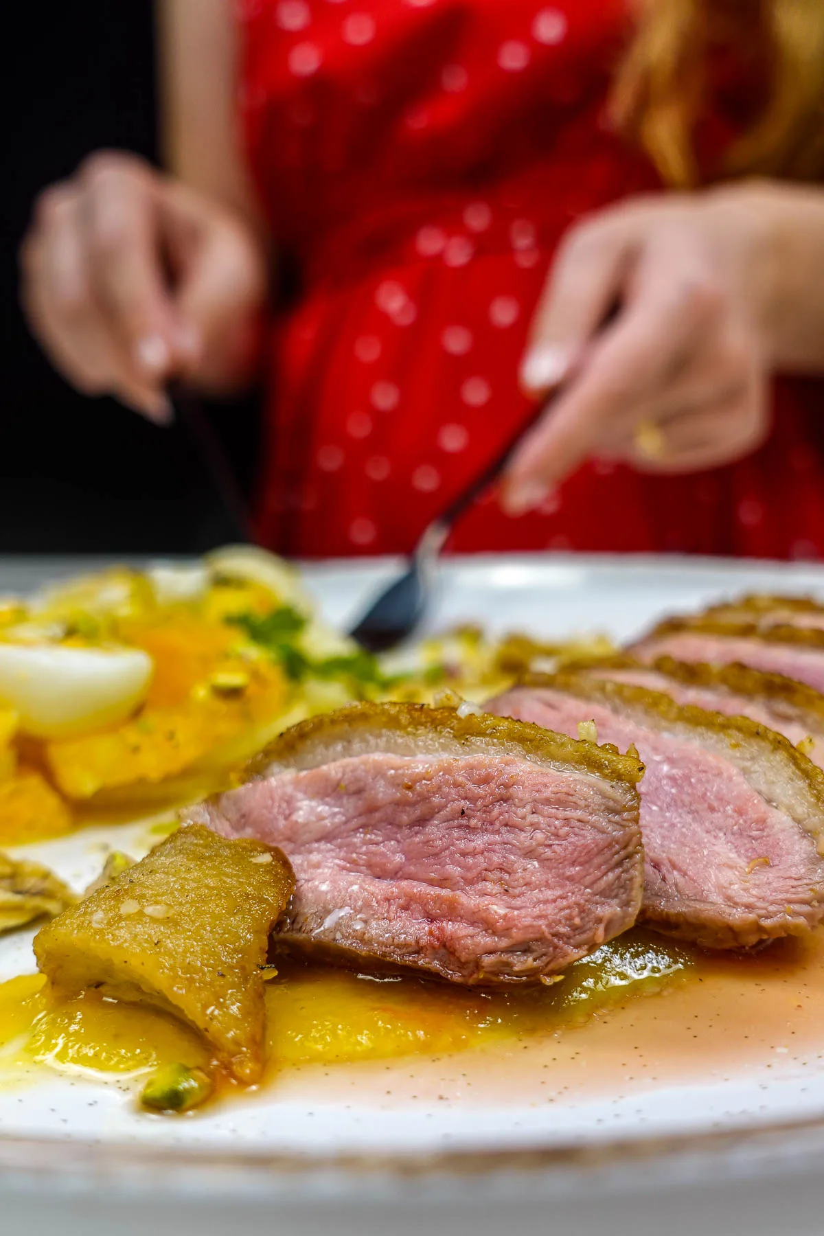 Helena is standing behind the plate with sliced crispy duck breast with orange and pineapple sauce on plate.