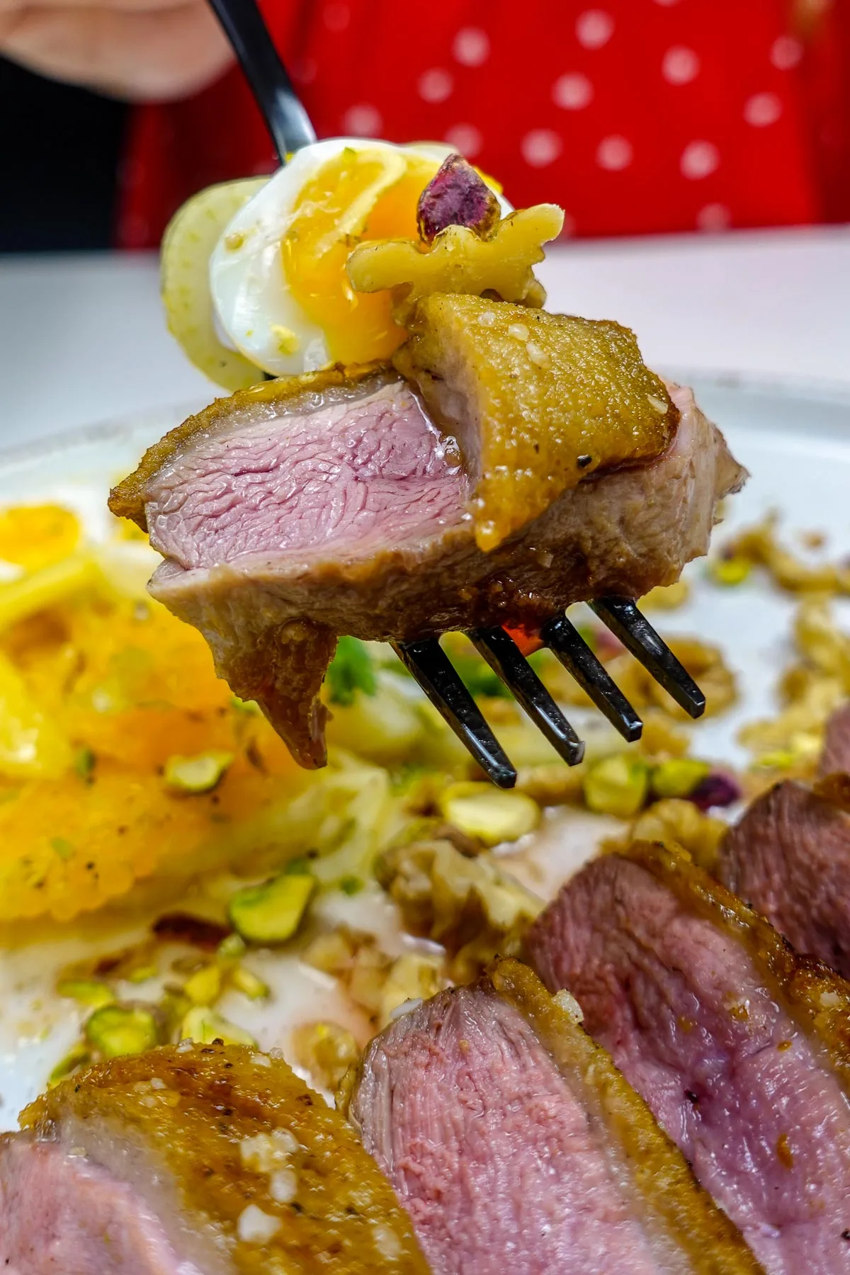 Helena is holding a fork with crispy duck breast with soft boiled egg and nuts.