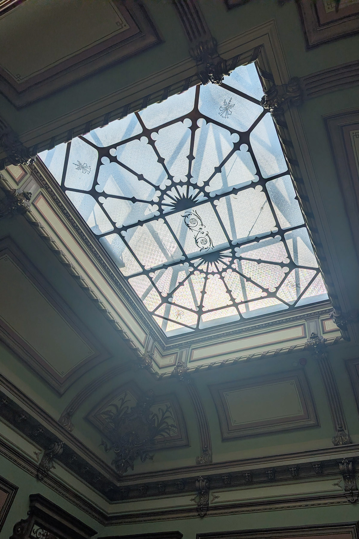 Ornate glass ceiling with decorative metal framework and intricate patterns.