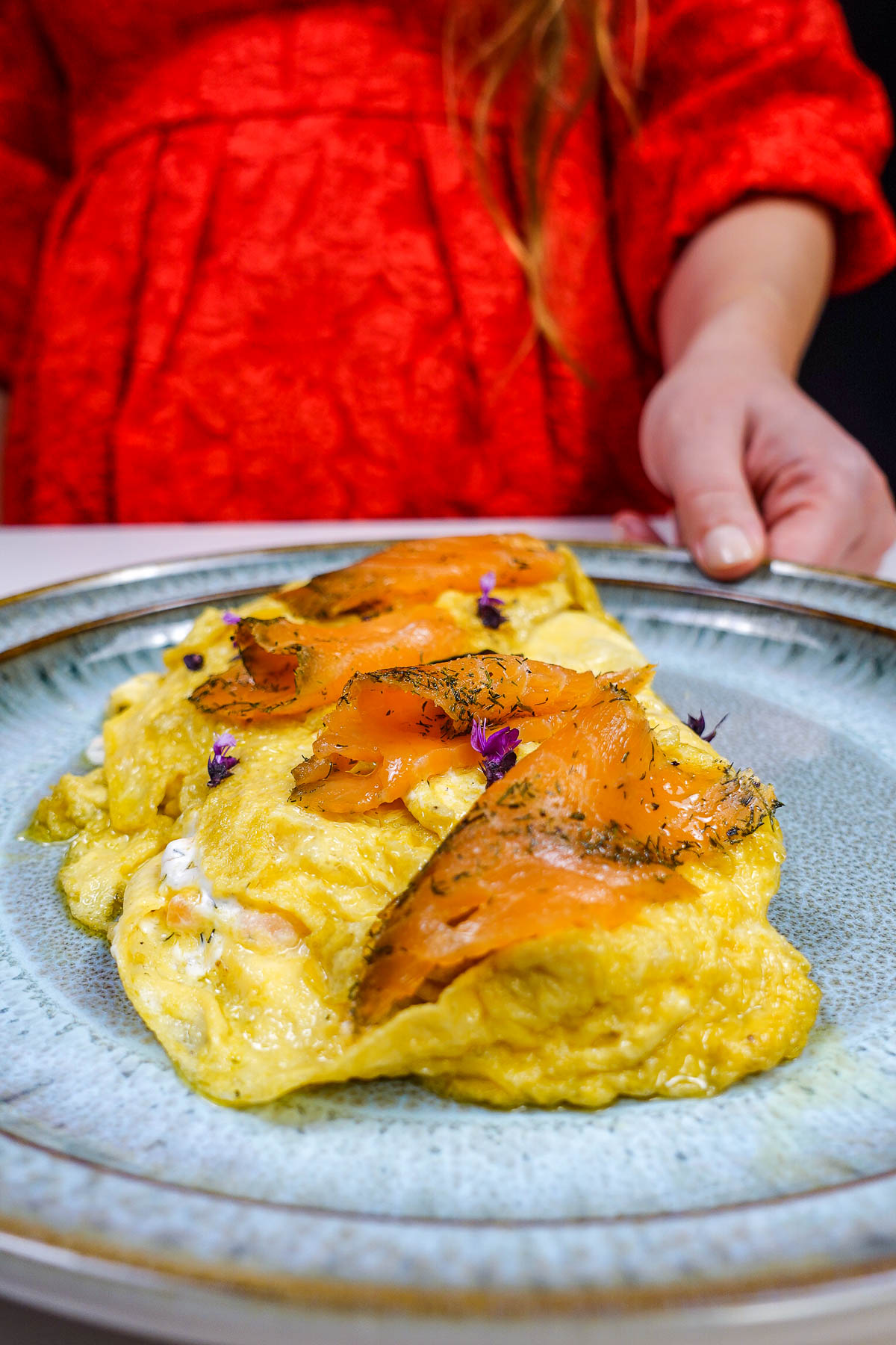 Smoked salmon topped omelette on a ceramic plate with purple flower garnishes.