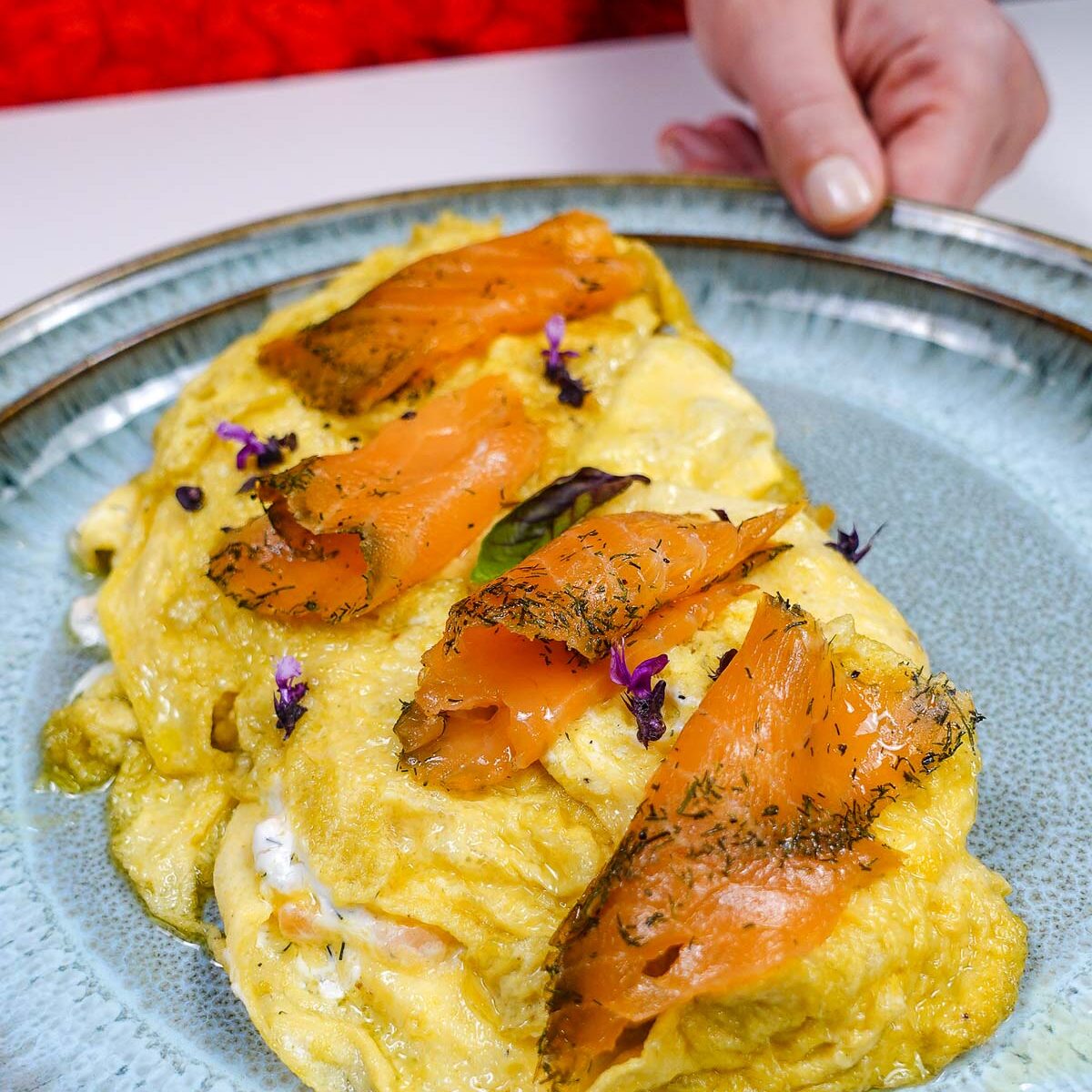 Smoked salmon topped omelette garnished with herbs and purple flowers.