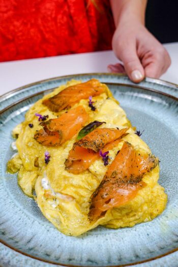 Smoked salmon topped omelette garnished with herbs and purple flowers.