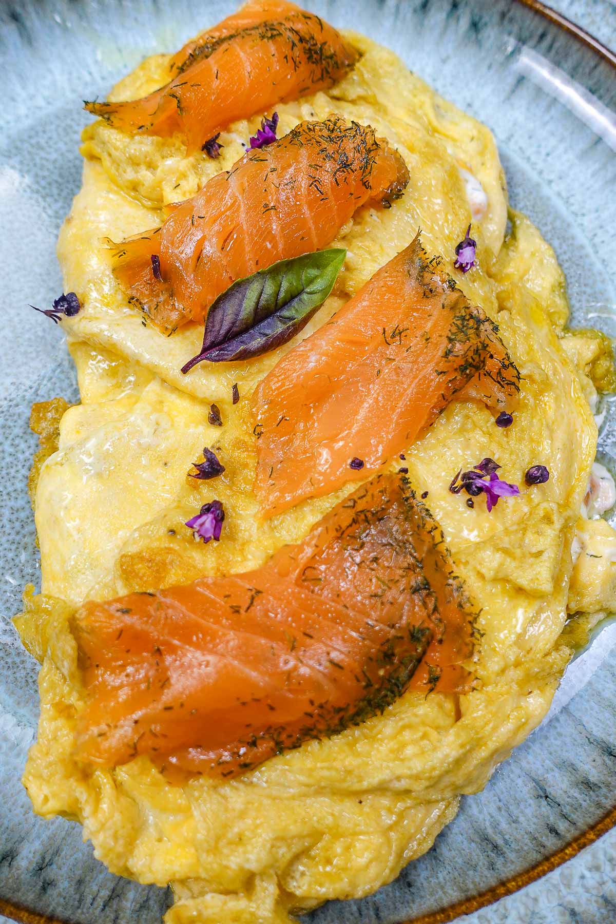Smoked salmon slices on a fluffy yellow omelette garnished with herbs.