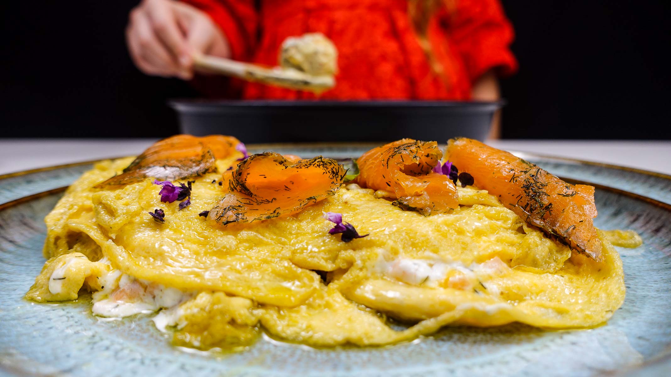 Smoked salmon topped omelette garnished with herbs and purple flowers.